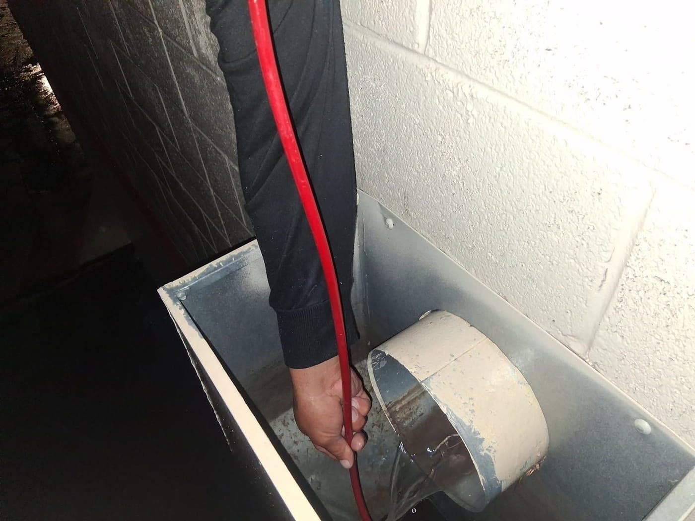 Technician feeding a drain-cleaning cable into a roof scupper box at night, with water flowing out