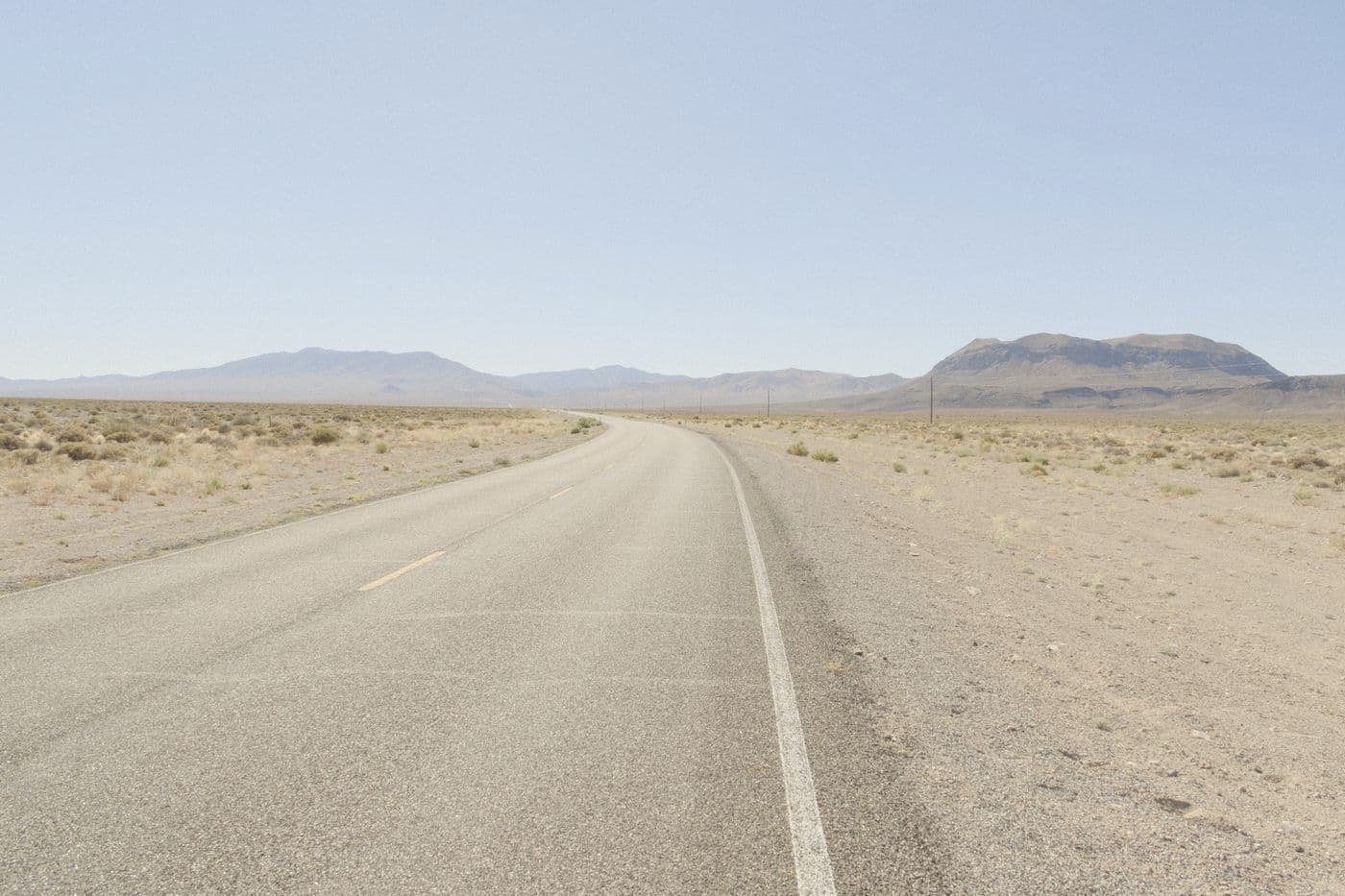 Empty two-lane highway crossing the Nevada desert toward mountains