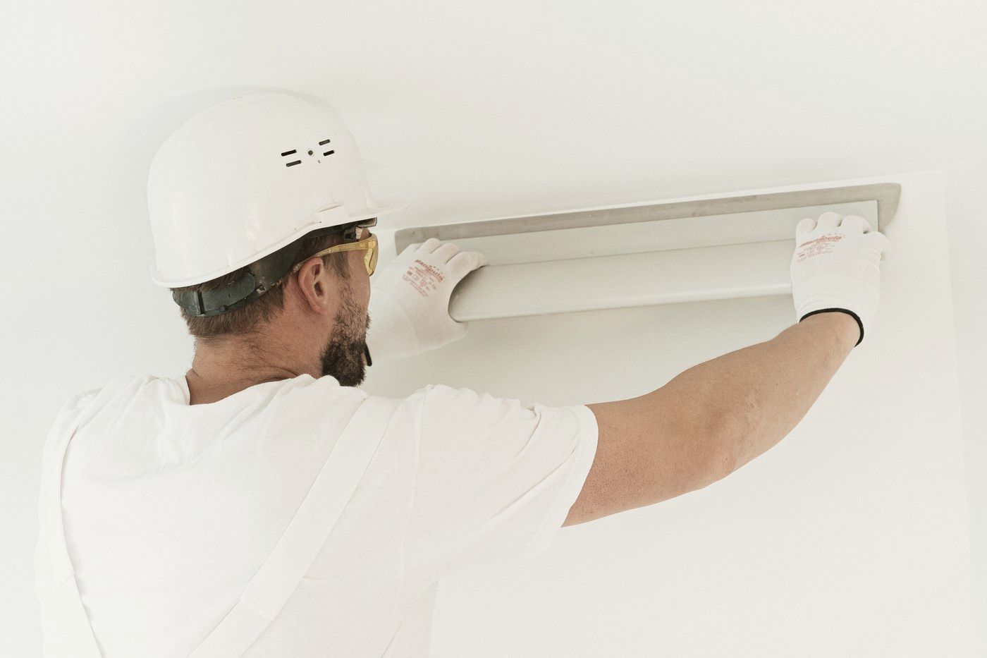 Technician in a hard hat installing a ceiling light fixture